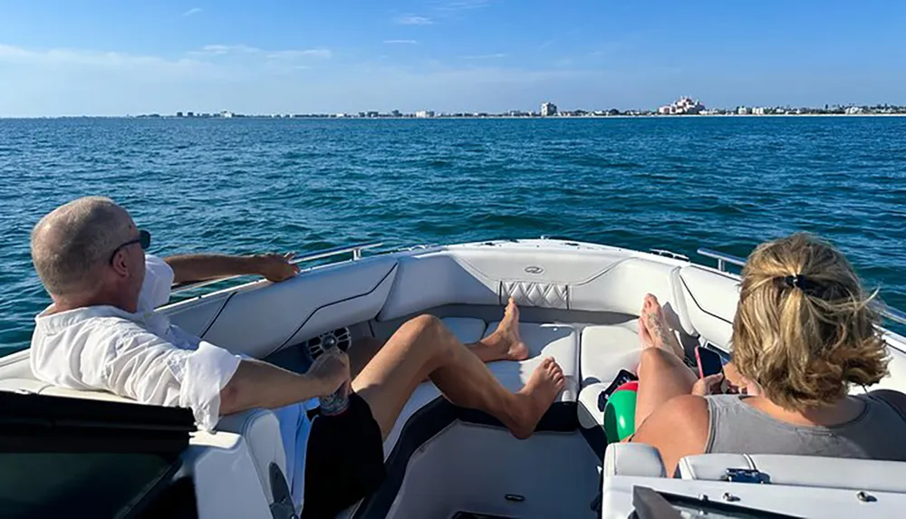 Two people are enjoying a boat ride on a sunny day with a clear view of the coastline in the distance