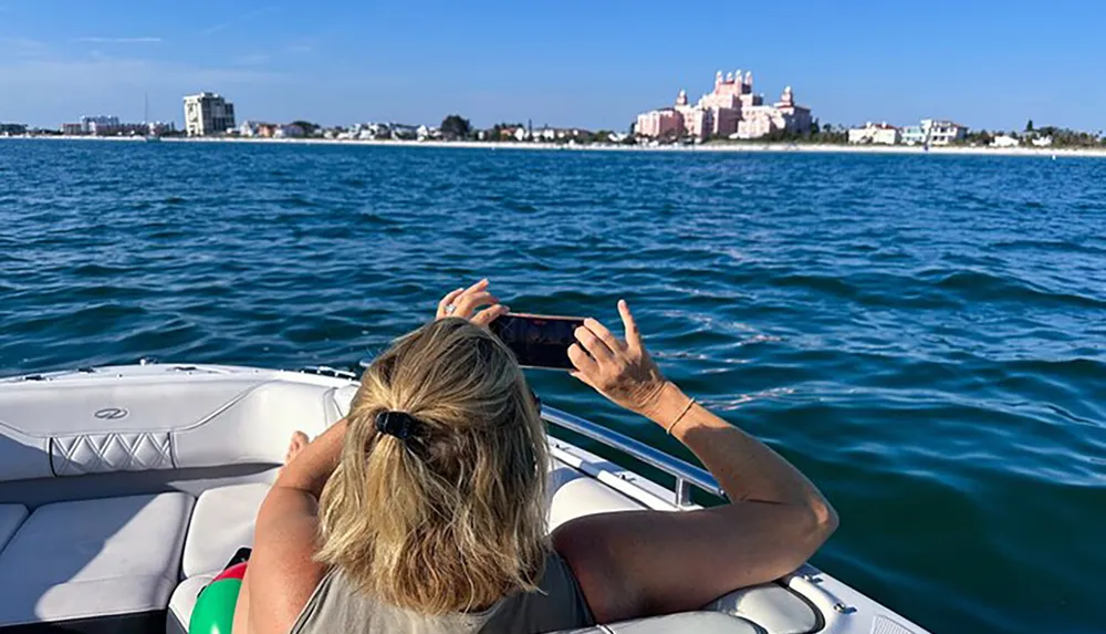 A person is taking a photo with their phone of a picturesque waterside building while lounging on a boat