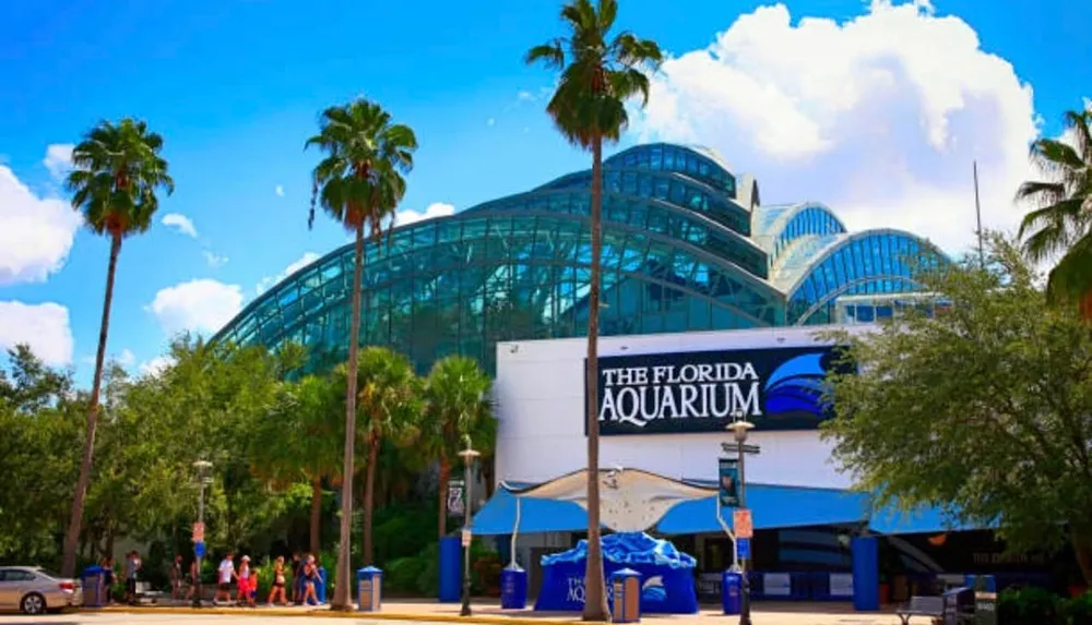 This is an image of the Florida Aquarium with its modern curved glass architecture surrounded by palm trees under a blue sky with fluffy clouds