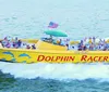 A yellow tour boat adorned with dolphin graphics speeds through the water with passengers on board with a large cable-stayed bridge visible in the background