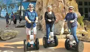 Three people are standing side by side outdoors, each on a Segway, with helmets on for safety, smiling for the camera.