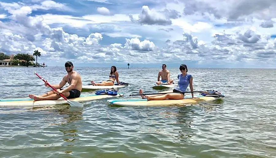 Four individuals are enjoying paddleboarding on a calm sea on a cloudy day.