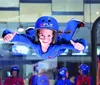 A person is enjoying an indoor skydiving experience with an instructor close by while onlookers watch from behind a glass partition