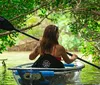 A person is kayaking through a serene waterway surrounded by greenery and overhanging branches