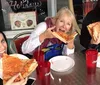 Three people are joyfully eating large slices of pizza at a table with drinks in red plastic cups