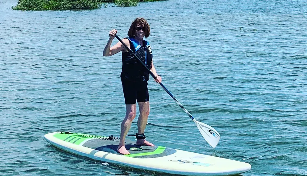 A person is stand-up paddleboarding on calm water holding a paddle mid-stroke