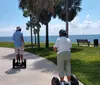 Three people are standing on Segways in front of a large striped sign that spells out TOYS with each person positioned inside one of the letters