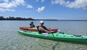 Two people are enjoying kayaking on clear, calm water with a beautiful sky overhead.