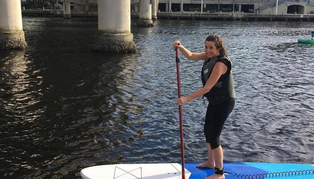 A person is stand-up paddleboarding on a body of water under a bridge