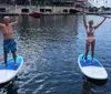 Two people are standing on paddleboards holding their paddles aloft on a calm water surface