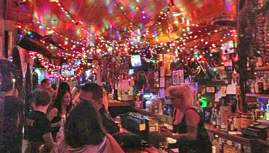 The image shows a bustling bar interior adorned with colorful string lights and patrons engaged in conversation.