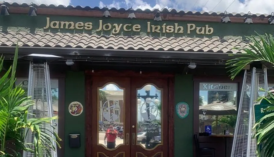 The image shows the front facade of James Joyce Irish Pub with a green exterior, brown double doors, and palm plants on either side.