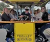 A group of people enjoys a ride on a pedal-powered Trolley Pub on a sunny day in an urban street setting