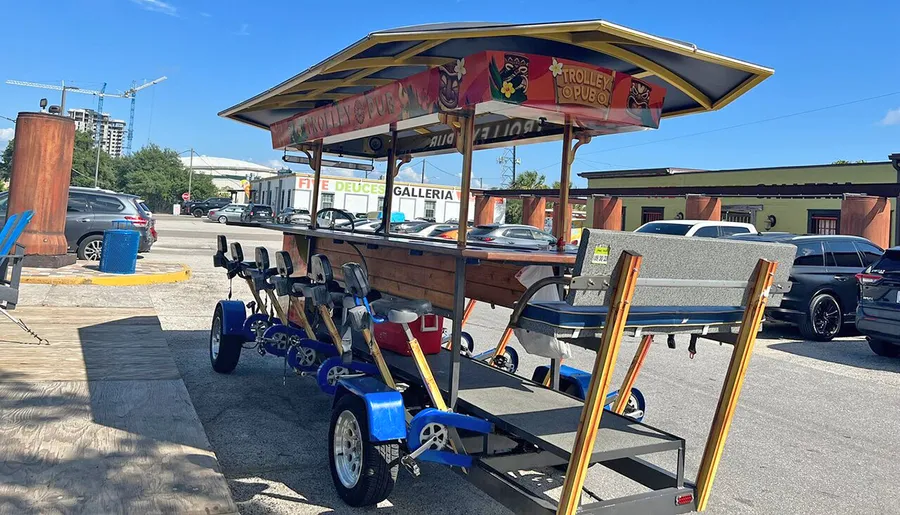 A pedal-powered trolley pub with multiple seats and bicycle pedals for each passenger is parked on a sunny day.