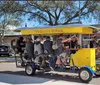 A group of people enjoys a ride on a pedal-powered Trolley Pub on a sunny day in an urban street setting