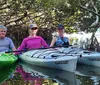 Three people are smiling while sitting on two kayaks among mangroves with calm waters reflecting the scene