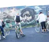 A group of cyclists are standing in front of a colorful intricate mural featuring psychedelic and vibrant imagery with the words Positive Creations and Peace Please