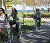 A group of people in orange shirts some with the University of Tennessee logo are riding or standing next to bicycles along a coastal area with palm trees and moored boats in the background