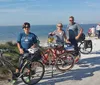 Three people are standing with their bicycles on a sunny day near a beach seemingly enjoying a break from cycling