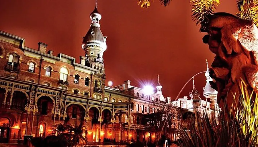 The image shows a dramatically lit, ornate building at night, with a close-up of a sculpted face in the foreground projecting a somewhat eerie ambiance.