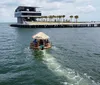 The image depicts a thatch-roofed floating tiki bar surrounded by clear turquoise waters under a blue sky with people enjoying the unique setting on the water