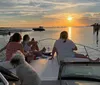 A group of individuals is enjoying a sunset on a boat with calm seas and a colorful sky in the background