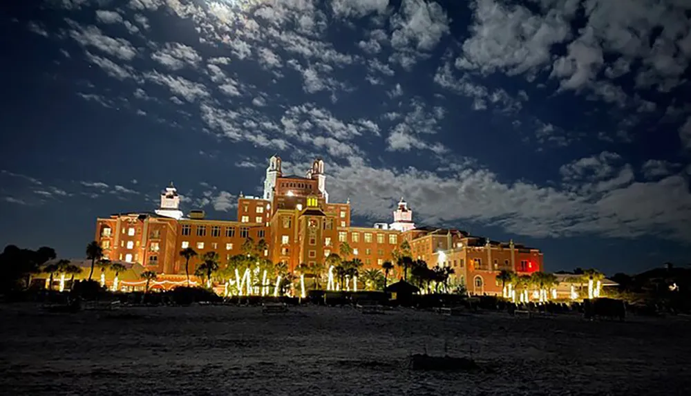 A grand illuminated building stands out against a night sky speckled with clouds