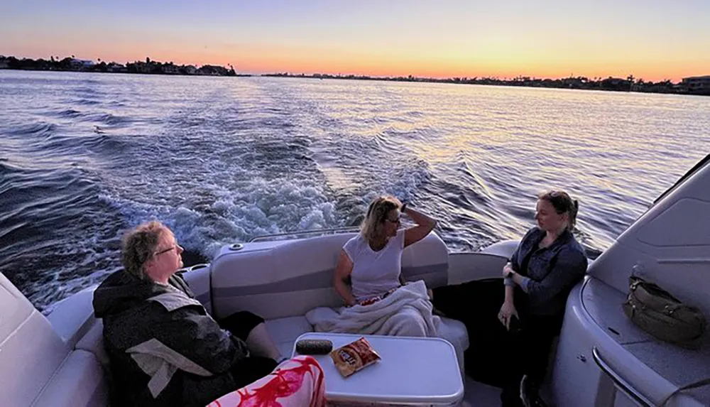 Three individuals are enjoying a boat ride during sunset creating a serene atmosphere with the water trailing behind them