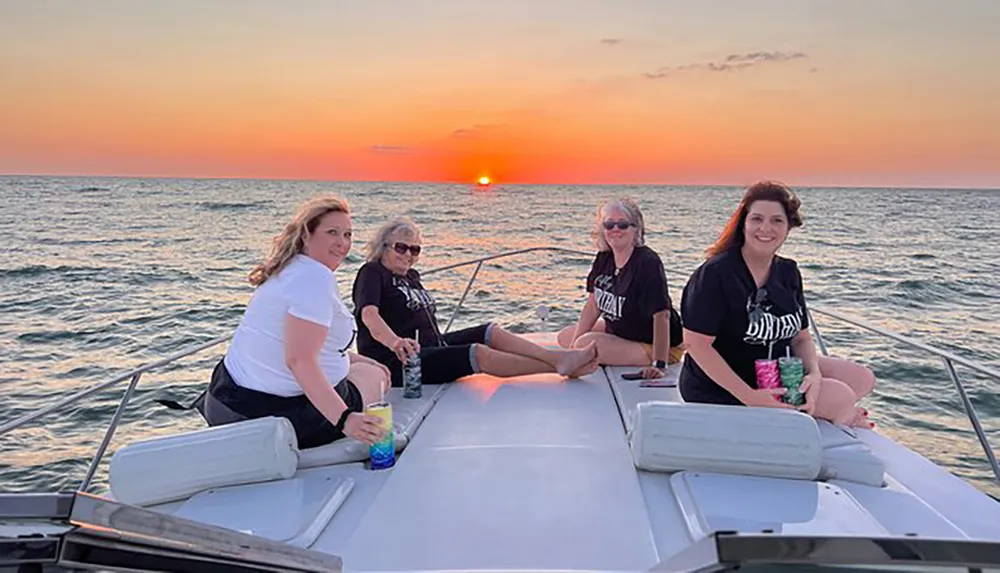 A group of individuals is enjoying a sunset on a boat with calm seas and a colorful sky in the background