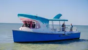 A novelty boat designed to look like a shark, complete with a gaping mouth, is carrying passengers on a clear day at sea.