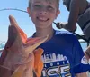 A man and a woman are smiling on a boat proudly displaying a large reddish fish they have caught