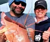 A man and a woman are smiling on a boat proudly displaying a large reddish fish they have caught