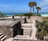 The image depicts an old concrete military fortification overlooking a tropical beach with palm trees and a clear blue sea