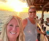 A smiling couple takes a selfie at a seaside bar with a beautiful sunset in the background