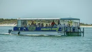 A ferry boat filled with passengers is cruising near a shoreline.