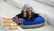 A joyful child slides down a snowy hill on a blue inflatable snow tube, wearing a winter jacket and a knitted hat.