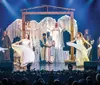 A group of performers in white costumes is dancing on stage in front of an audience with festive holiday decorations around them