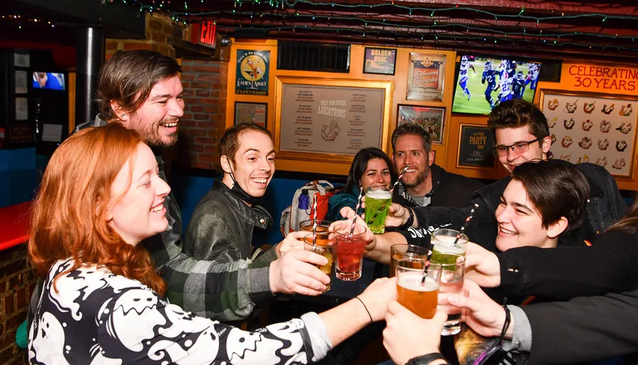 A group of cheerful people are toasting drinks together in a lively bar setting.