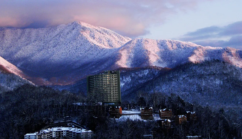 A tall building stands out against a backdrop of snow-covered mountains bathed in the warm glow of sunrise or sunset
