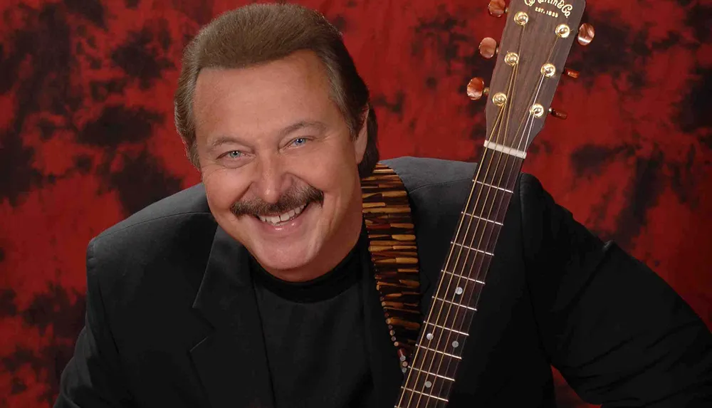 A smiling person holding a guitar poses against a red and black textured background