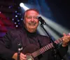 A smiling musician is playing the guitar on stage with colorful lights in the background