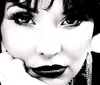 The image features a close-up black-and-white portrait of a woman with a vintage hairstyle dark lipstick and intense gaze resting her chin on her hand