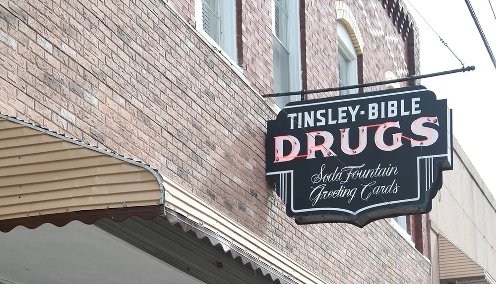 The image shows a vintage-style sign for Tinsley-Bible Drugs mentioning a soda fountain and greeting cards mounted on a brick building