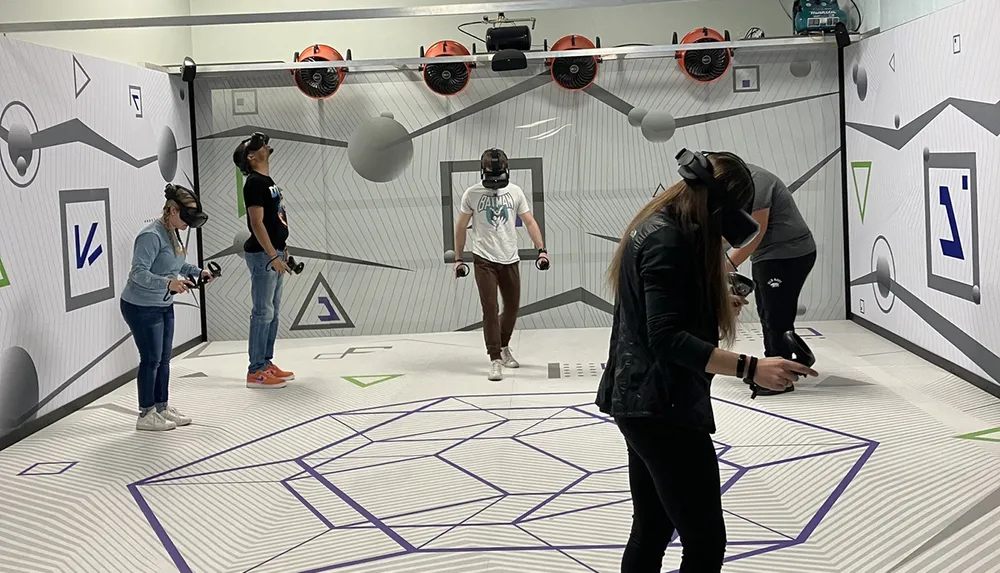 Four people are wearing virtual reality headsets and using handheld controllers seemingly immersed in a virtual reality experience in a room with specialized tracking equipment