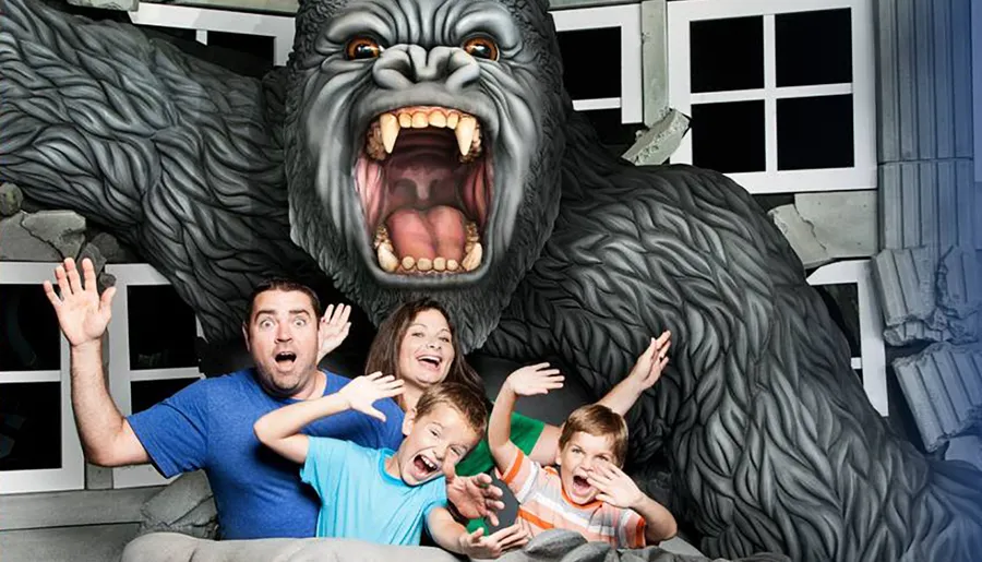 A family is posing with exaggerated expressions of fear as if they are being attacked by a large gorilla, in what looks to be a staged amusement park photo opportunity.