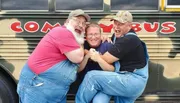 Three jovial men are posing playfully in front of a bus, showing a great sense of camaraderie and humor.