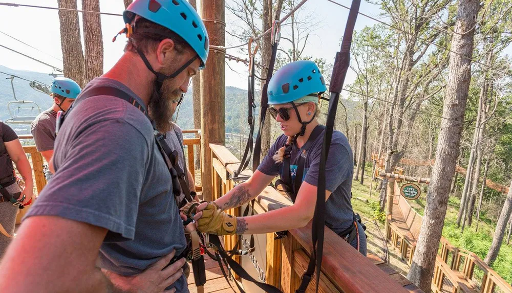 People wearing safety helmets and harnesses are preparing to participate in an outdoor ziplining or ropes course adventure