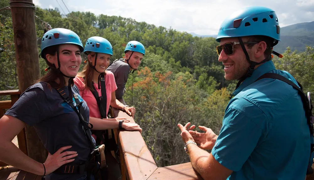 A group of people wearing safety helmets and harnesses are enjoying a conversation in an outdoor setting likely preparing for or having finished an adventure sport such as zip-lining