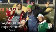 Four joyful people dressed in festive Christmas attire posing in front of a bus named 