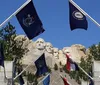 The image shows a view of the Mount Rushmore National Memorial with the carved faces of four American presidents framed by an array of state flags